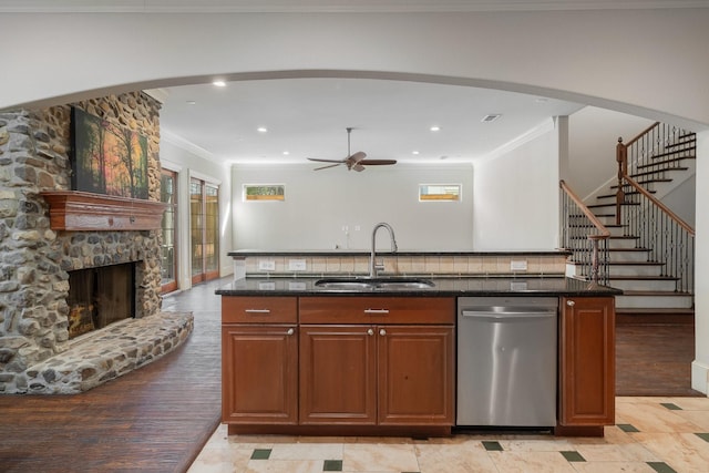 kitchen with stainless steel dishwasher, ceiling fan, a kitchen island with sink, sink, and a fireplace