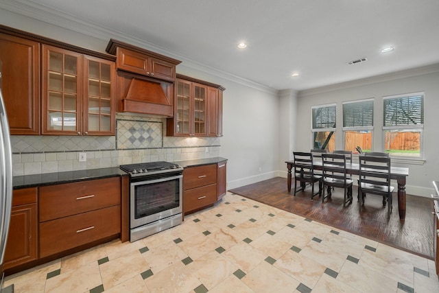 kitchen featuring stainless steel range oven, premium range hood, dark stone countertops, crown molding, and light wood-type flooring