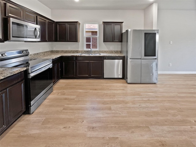 kitchen featuring light stone countertops, appliances with stainless steel finishes, dark brown cabinetry, sink, and light hardwood / wood-style flooring