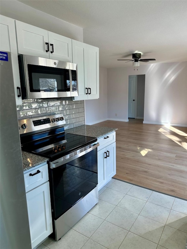 kitchen featuring stainless steel appliances, white cabinets, ceiling fan, and dark stone counters