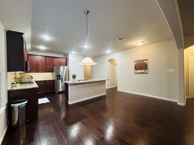 kitchen featuring light stone counters, stainless steel appliances, sink, decorative light fixtures, and an island with sink