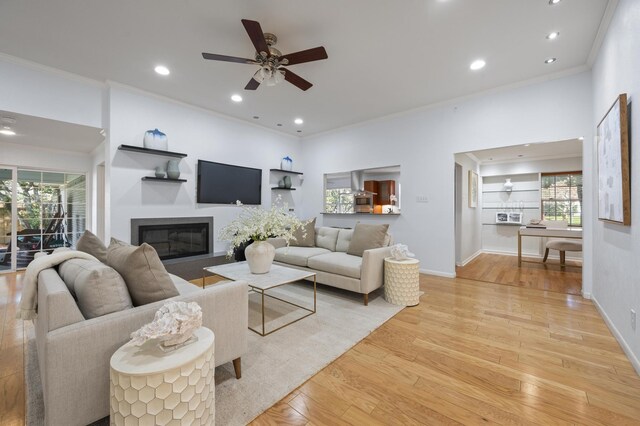 living room with ceiling fan, light wood-type flooring, ornamental molding, and a wealth of natural light