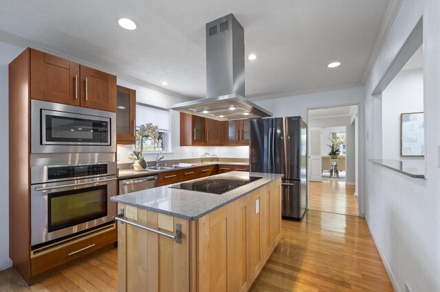 kitchen with island exhaust hood, appliances with stainless steel finishes, light stone counters, crown molding, and a center island