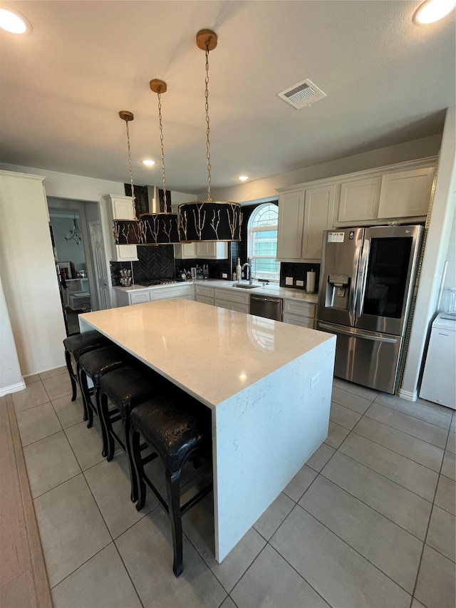 kitchen featuring light tile patterned flooring, a center island, hanging light fixtures, appliances with stainless steel finishes, and a kitchen breakfast bar