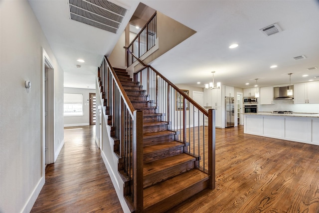 stairway featuring wood-type flooring and an inviting chandelier