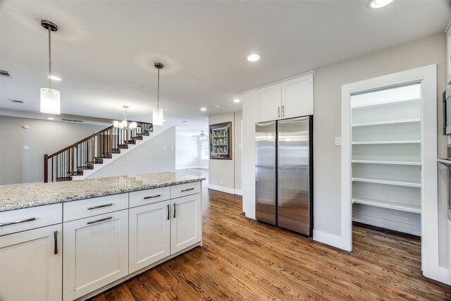 kitchen with stainless steel refrigerator, white cabinetry, hanging light fixtures, light stone counters, and wood-type flooring