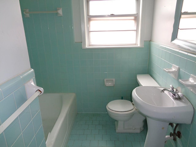 bathroom featuring toilet, tile patterned floors, tile walls, and a tub