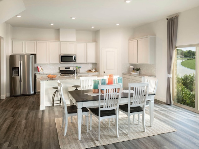 kitchen with appliances with stainless steel finishes, tasteful backsplash, a kitchen island with sink, white cabinets, and dark hardwood / wood-style floors