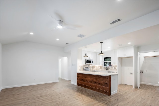 kitchen with white cabinets, appliances with stainless steel finishes, decorative light fixtures, and light hardwood / wood-style flooring