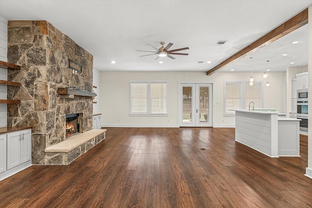 unfurnished living room featuring a fireplace, beamed ceiling, dark hardwood / wood-style flooring, ceiling fan, and french doors