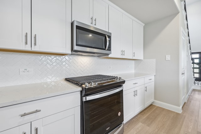 kitchen with decorative backsplash, light stone countertops, light wood-type flooring, appliances with stainless steel finishes, and white cabinetry