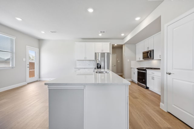 kitchen with white cabinets, an island with sink, light hardwood / wood-style floors, and appliances with stainless steel finishes