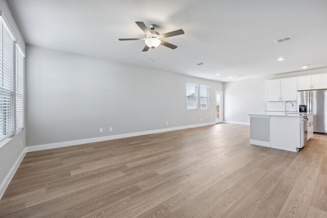 unfurnished living room with light hardwood / wood-style flooring, ceiling fan, and sink