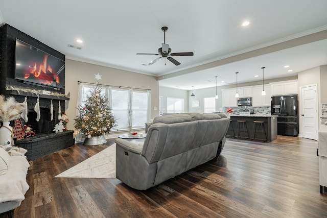 living room with dark hardwood / wood-style floors, a brick fireplace, ceiling fan, and crown molding