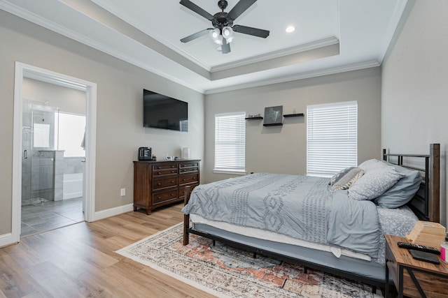 bedroom with light wood-type flooring, ensuite bathroom, a tray ceiling, ceiling fan, and crown molding