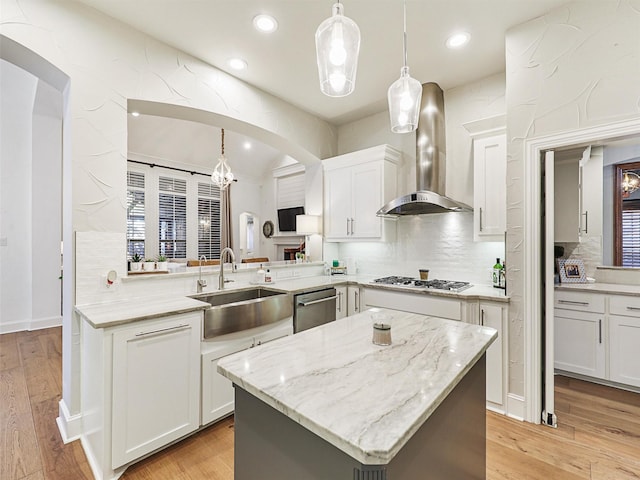 kitchen with kitchen peninsula, hanging light fixtures, wall chimney exhaust hood, and sink