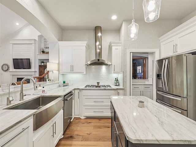 kitchen with light stone counters, white cabinets, wall chimney range hood, and appliances with stainless steel finishes