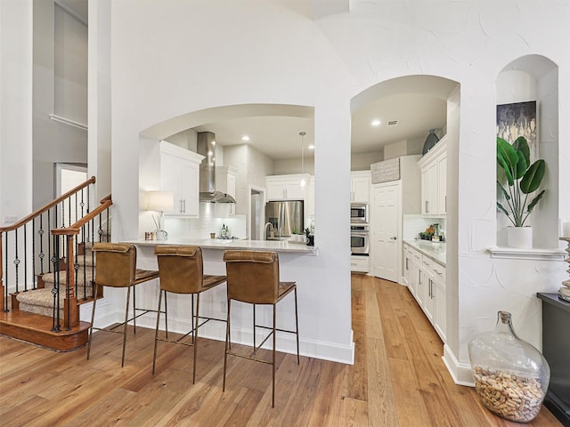 kitchen with white cabinets, stainless steel appliances, and wall chimney range hood