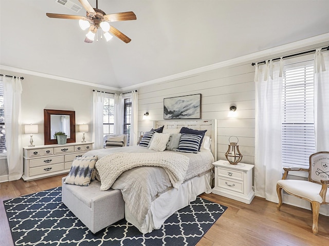 bedroom with ceiling fan, light wood-type flooring, ornamental molding, and wooden walls