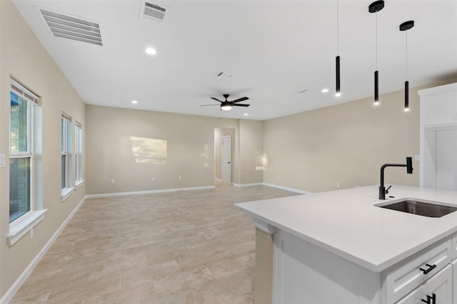 kitchen featuring pendant lighting, a kitchen island with sink, white cabinets, sink, and ceiling fan