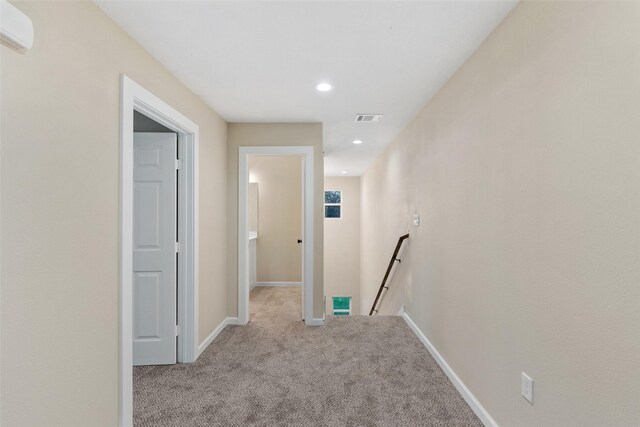 corridor featuring a wall mounted air conditioner and light colored carpet