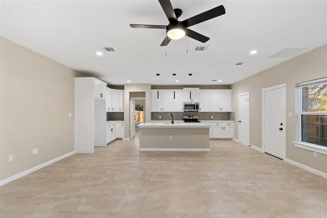 kitchen with a kitchen island with sink, hanging light fixtures, ceiling fan, appliances with stainless steel finishes, and white cabinetry