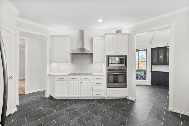 kitchen with wall chimney range hood, ornamental molding, tasteful backsplash, white cabinetry, and stainless steel appliances