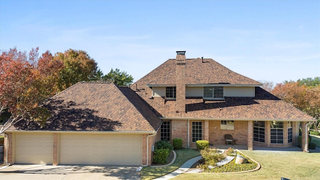 traditional-style house with a garage, a chimney, roof with shingles, a front lawn, and brick siding