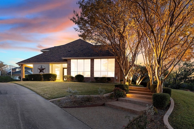 view of front of home with a front lawn, brick siding, and roof with shingles
