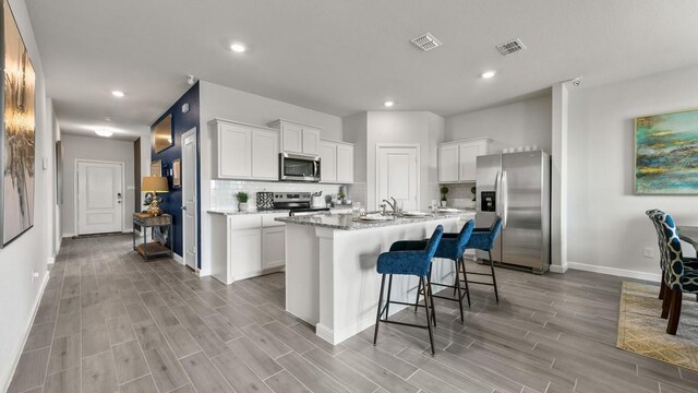 kitchen featuring white cabinetry, a kitchen island with sink, stainless steel appliances, and light stone counters