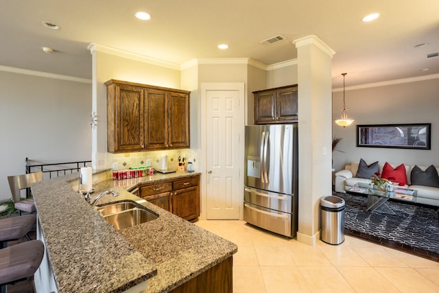 kitchen with kitchen peninsula, stainless steel refrigerator with ice dispenser, a kitchen bar, tasteful backsplash, and sink