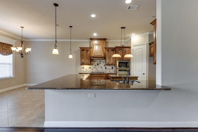 kitchen featuring dark stone counters, custom range hood, stainless steel appliances, a notable chandelier, and hanging light fixtures