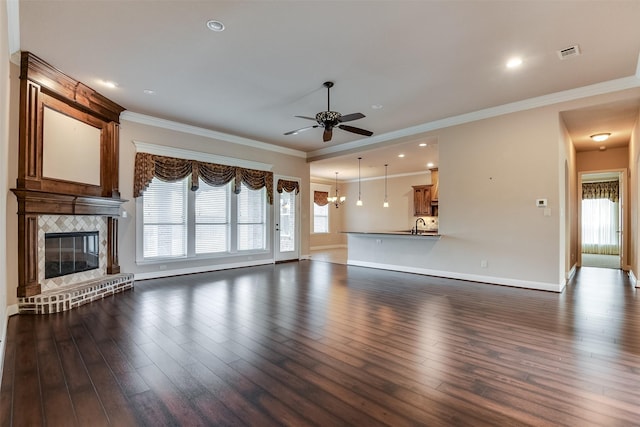 unfurnished living room with a large fireplace, dark wood-type flooring, ceiling fan with notable chandelier, and ornamental molding