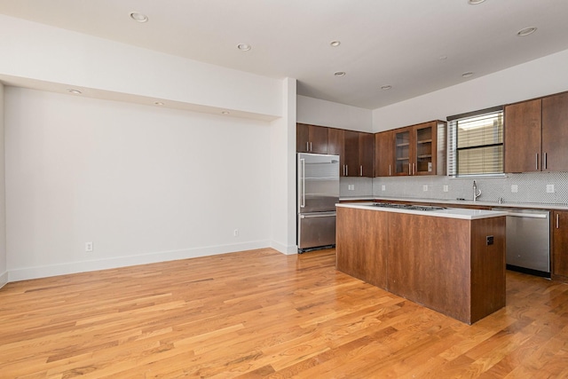 kitchen with backsplash, stainless steel appliances, a kitchen island, and light hardwood / wood-style flooring