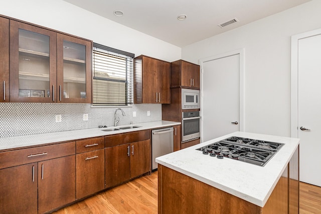 kitchen with sink, light hardwood / wood-style flooring, decorative backsplash, a kitchen island, and stainless steel appliances