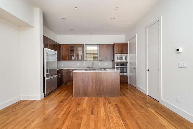 kitchen with tasteful backsplash, built in appliances, a center island, and light hardwood / wood-style floors