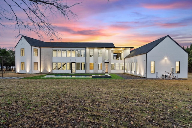 back house at dusk featuring a yard and a balcony