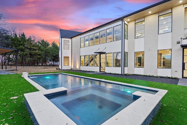 pool at dusk with an in ground hot tub and a yard