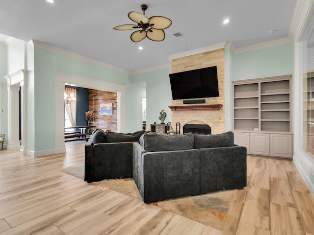 living room featuring ceiling fan with notable chandelier, a large fireplace, light hardwood / wood-style flooring, and ornamental molding