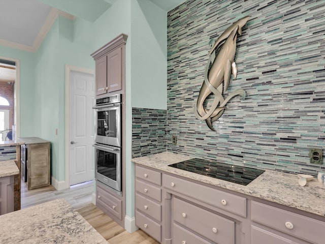 kitchen featuring stainless steel double oven, black electric stovetop, backsplash, light stone counters, and light hardwood / wood-style flooring