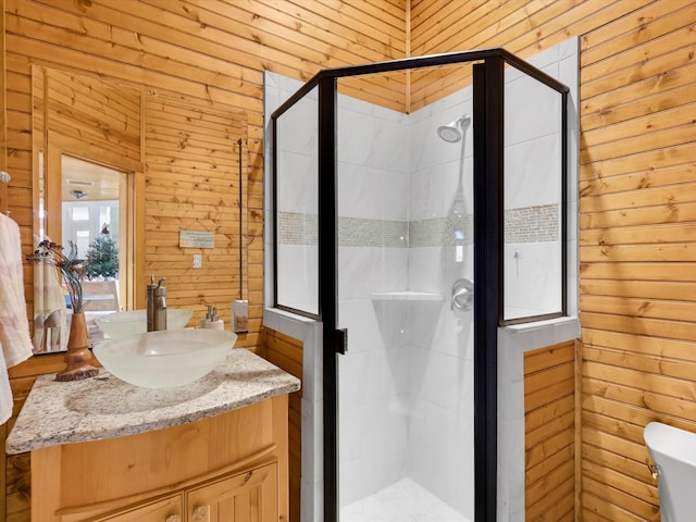 bathroom with a shower with shower door, vanity, toilet, and wood walls