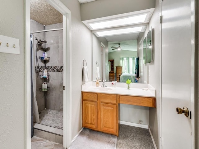 bathroom with a skylight, vanity, tiled shower, ceiling fan, and a textured ceiling