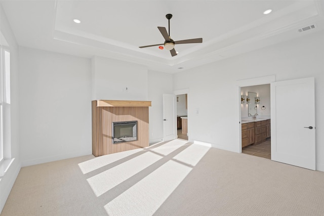 unfurnished bedroom featuring ceiling fan, a raised ceiling, light carpet, and connected bathroom