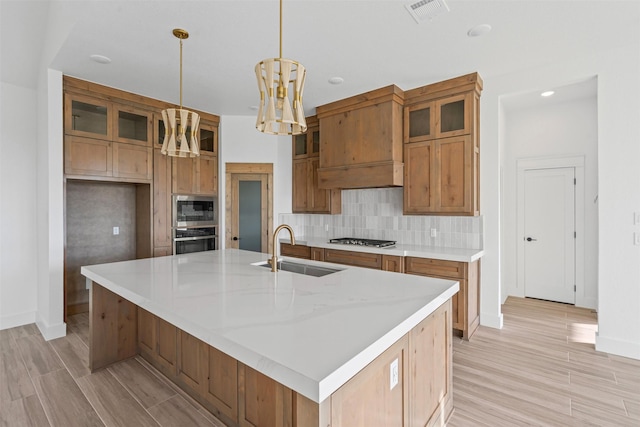 kitchen featuring stainless steel appliances, sink, pendant lighting, a center island with sink, and light hardwood / wood-style floors