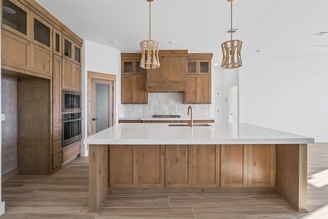 kitchen with sink, light hardwood / wood-style flooring, decorative light fixtures, a kitchen island with sink, and appliances with stainless steel finishes