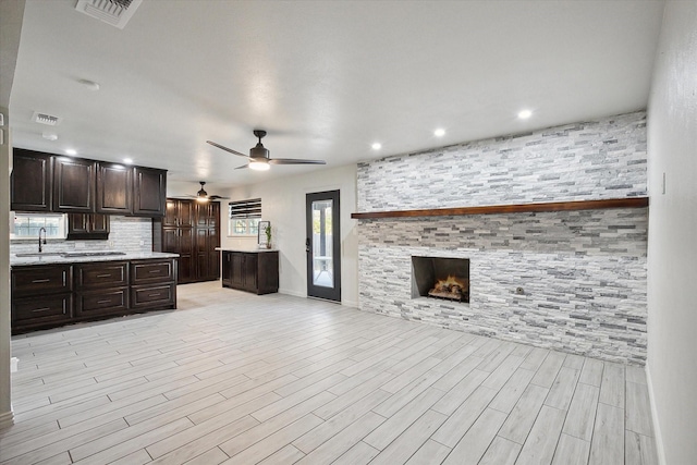 kitchen with sink, dark brown cabinets, light wood-type flooring, ceiling fan, and a fireplace