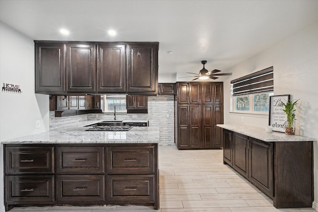 kitchen with dark brown cabinets, light stone counters, ceiling fan, and kitchen peninsula