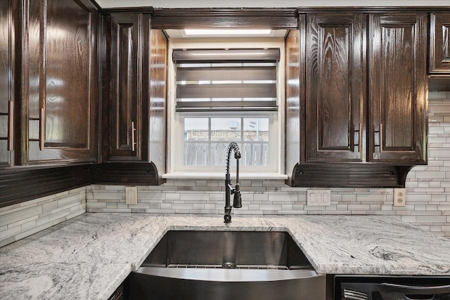 kitchen featuring light stone countertops, dark brown cabinets, sink, and decorative backsplash