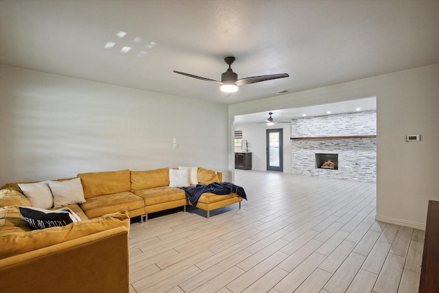 living room featuring ceiling fan, a fireplace, and light wood-type flooring