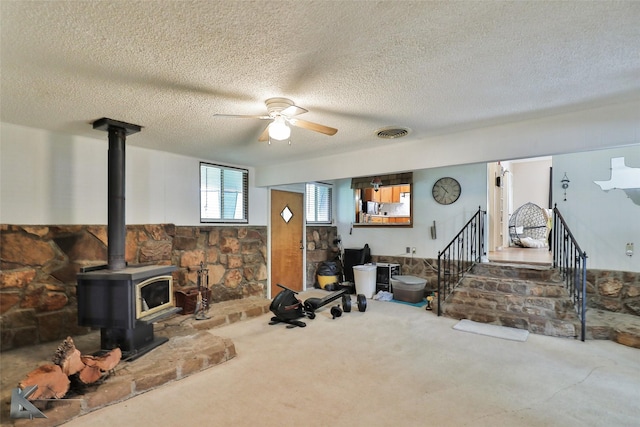 living room with carpet, a textured ceiling, a wood stove, and ceiling fan